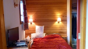 A bedroom with a wooden headboard, a bed with a red blanket, bedside lamps, a desk with a computer, and a wardrobe.