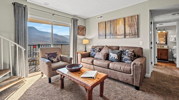A living room with a sofa, armchair, and coffee table, a balcony with curtains, and a view of mountains. - Sleeps 6 Mountain Views Shared Resort Amenities (Gatlinburg)
