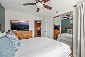 Ein Schlafzimmer mit Bett, Deckenventilator, Fernseher und Kleiderschrank.