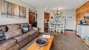 A living room with a brown leather sofa, a coffee table with a bowl of remotes, a dining area with a white table and chairs, and a kitchen in the background. - Sleeps 6 Mountain Views Shared Resort Amenities (Gatlinburg)