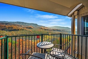 Un balcon avec une table et des chaises, donnant sur un paysage montagneux aux couleurs automnales.