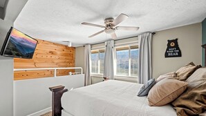 A bedroom with a bed, a ceiling fan, a mounted TV, and a wall with a bear-themed sign. - Sleeps 6 Mountain Views Shared Resort Amenities (Gatlinburg)