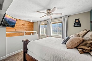 A bedroom with a bed, a ceiling fan, a mounted TV, and a wall with a bear-themed sign.