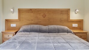 Cama com cabeceira de madeira, duas mesas de cabeceira e luminárias fixadas na parede.