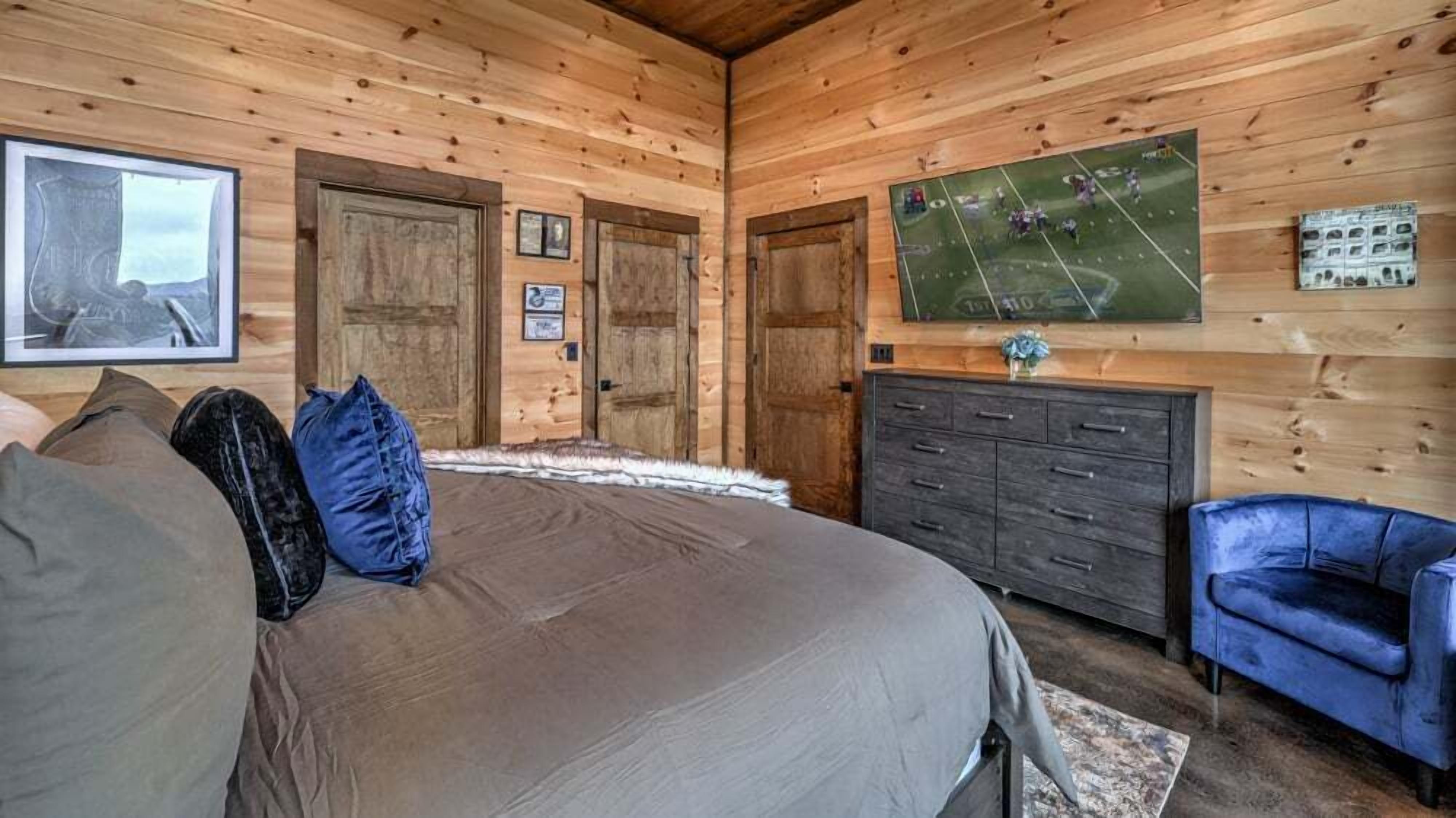Ein Zimmer mit Holzwänden, einem Bett, einem Schminktisch, einem Sessel und einem an der Wand montierten Fernseher.