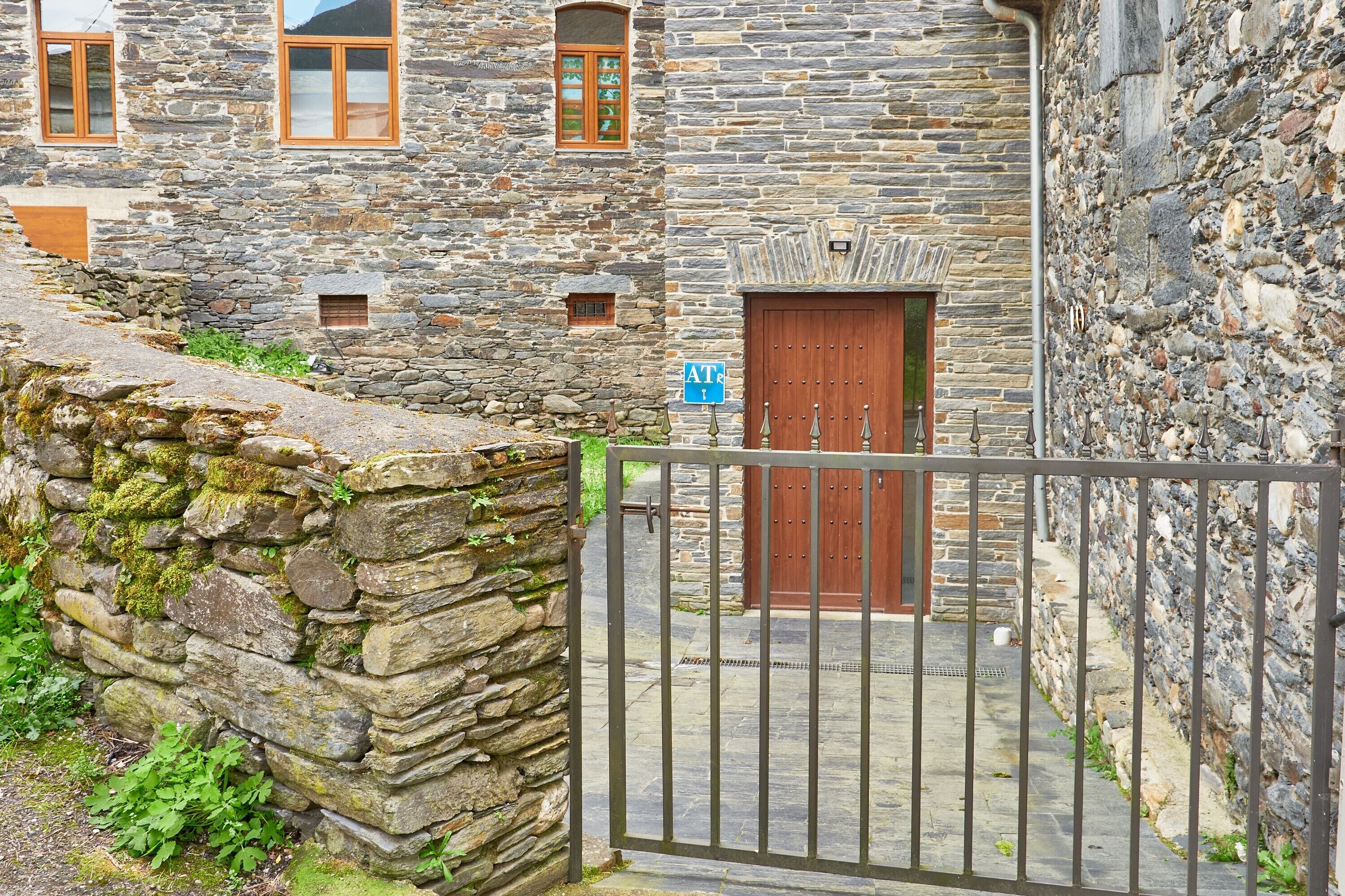 A stone building with a wooden door, a metal gate, and a small blue sign.