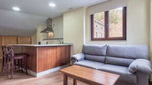 Una sala de estar con un sofá, una mesa de centro de madera, una zona de cocina con mostrador y una ventana con vistas a un edificio.