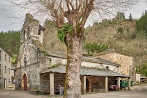 A stone building with a bell tower, a covered porch, and a tree in front.
