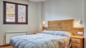 Ein Schlafzimmer mit einem Bett, einem Holzkopfteil, Nachttischen, einem Fenster mit Blick und einer Heizung.