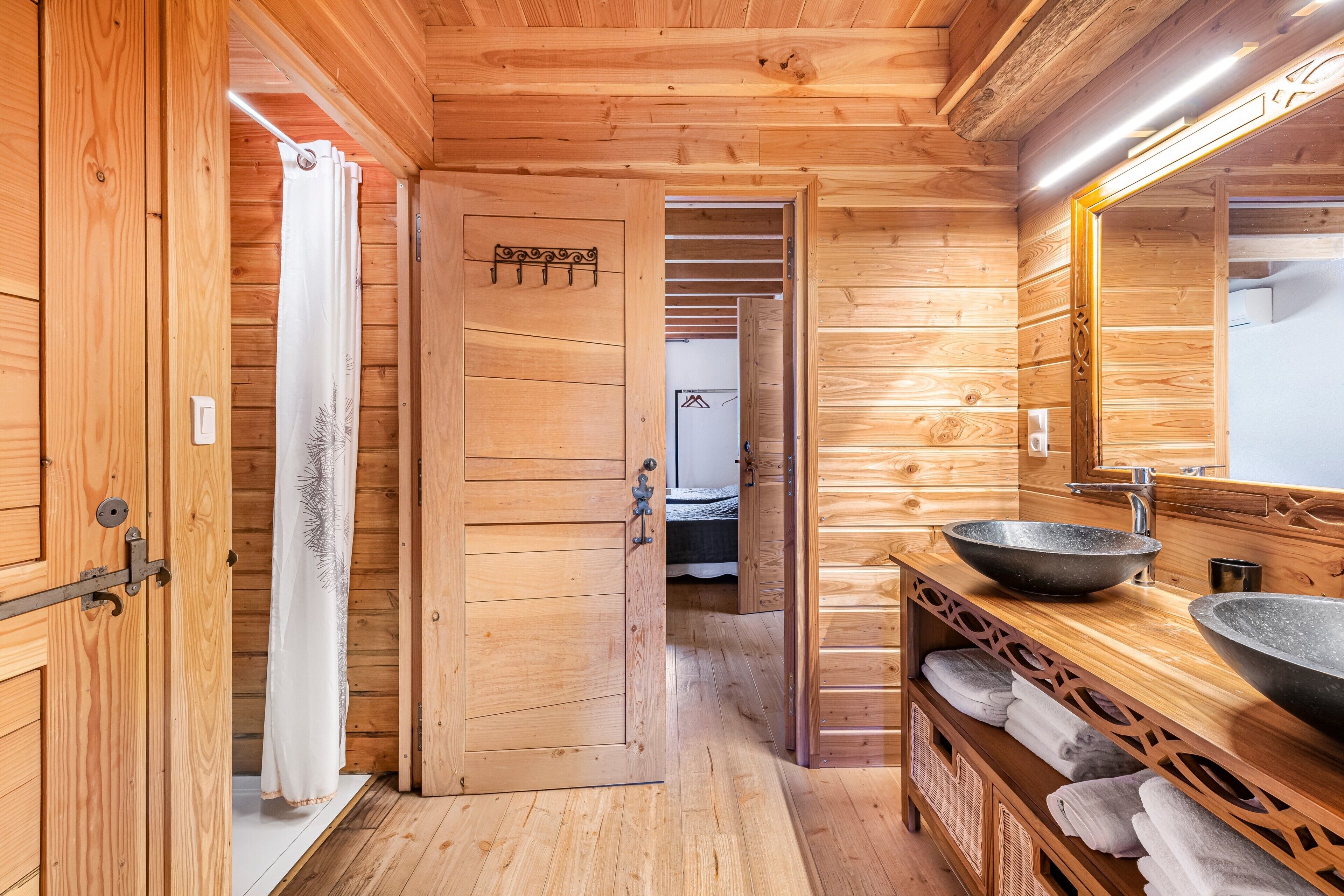 A wooden cabin interior with a wooden door, a bathroom with a sink and mirror, and a towel rack.