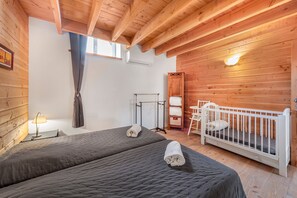 Una stanza con due letti, una culla, una lampada, una finestra con tende e pareti in legno.