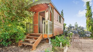 A wooden cabin with a porch, steps leading up to the entrance, and a small garden area. - Spacious, Bright and Welcoming Gîte with Mountain View, Private Terrace and Air Conditioning (Beaujeu)