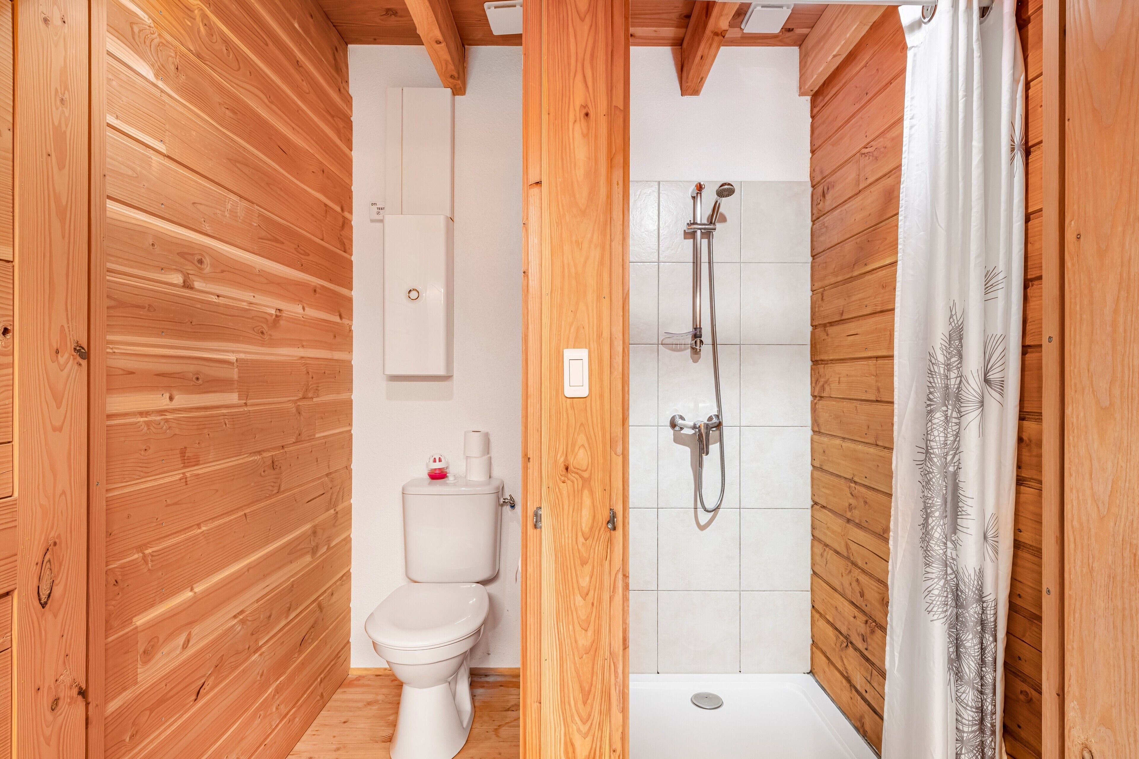 Ein Badezimmer mit Holzwandverkleidung, Toilette, Dusche und einem weißen Vorhang.