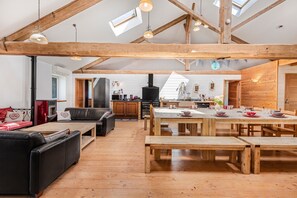 Un'ampia zona giorno con soffitto in legno, camino, tavolo da pranzo per quattro persone e un'accogliente angolo salotto.