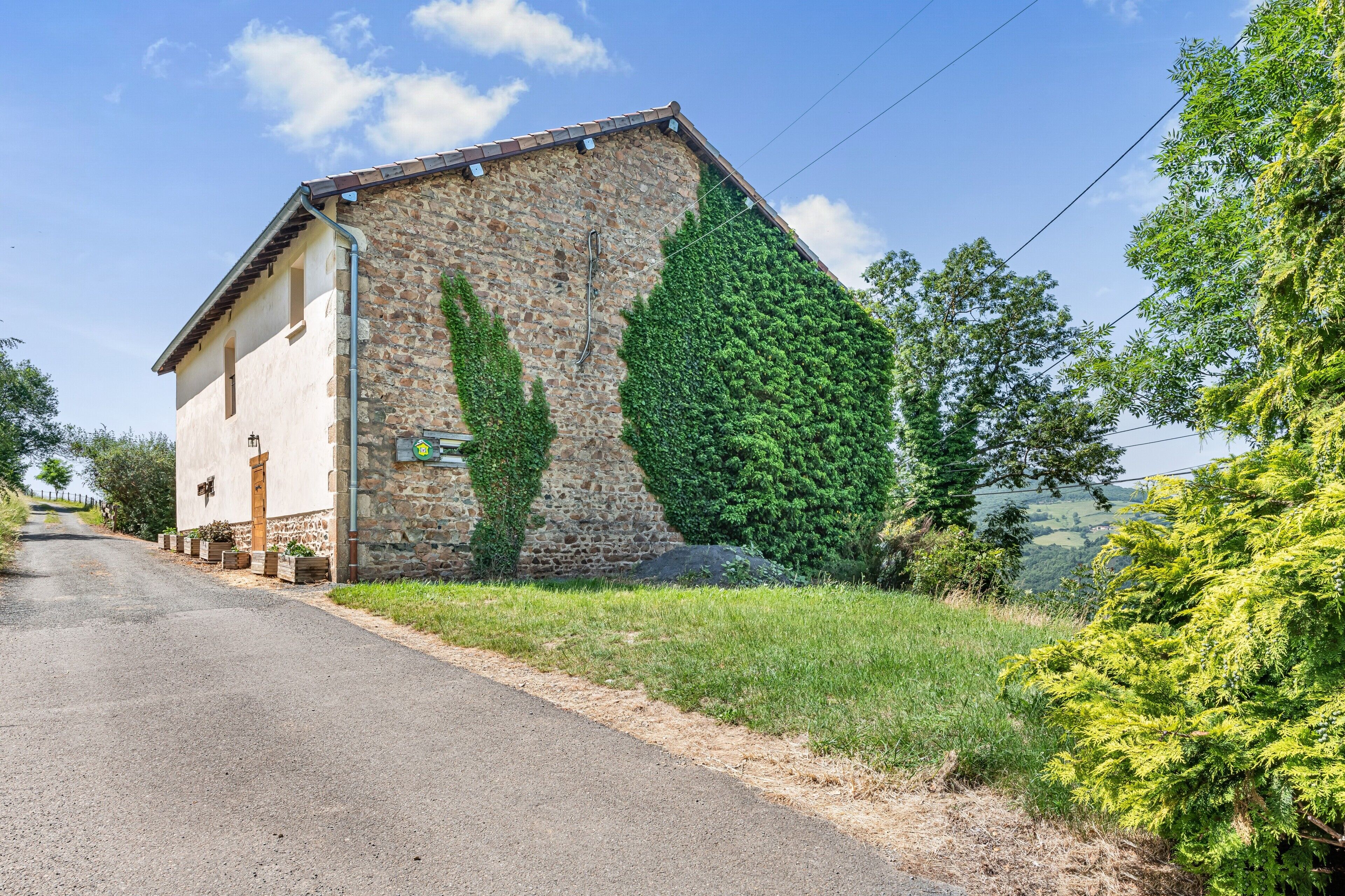 Ein Steinhaus mit geneigtem Dach, einer kleinen Veranda und einer Straße davor.