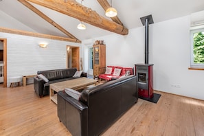 Um quarto amplo com teto de madeira, lareira, conjunto de sofás e mesa de jantar.