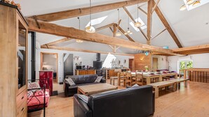 A spacious loft with exposed wooden beams, a kitchen, dining area, and a cozy seating area with a sofa and benches. - Spacious, Bright and Welcoming Gîte with Mountain View, Private Terrace and Air Conditioning (Beaujeu)