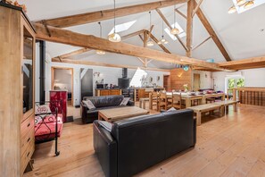 A spacious loft with high ceilings, exposed wooden beams, a kitchen, dining area, and a cozy seating area with a sofa and benches. - Spacious, Bright and Welcoming Gîte with Mountain View, Private Terrace and Air Conditioning (Beaujeu)