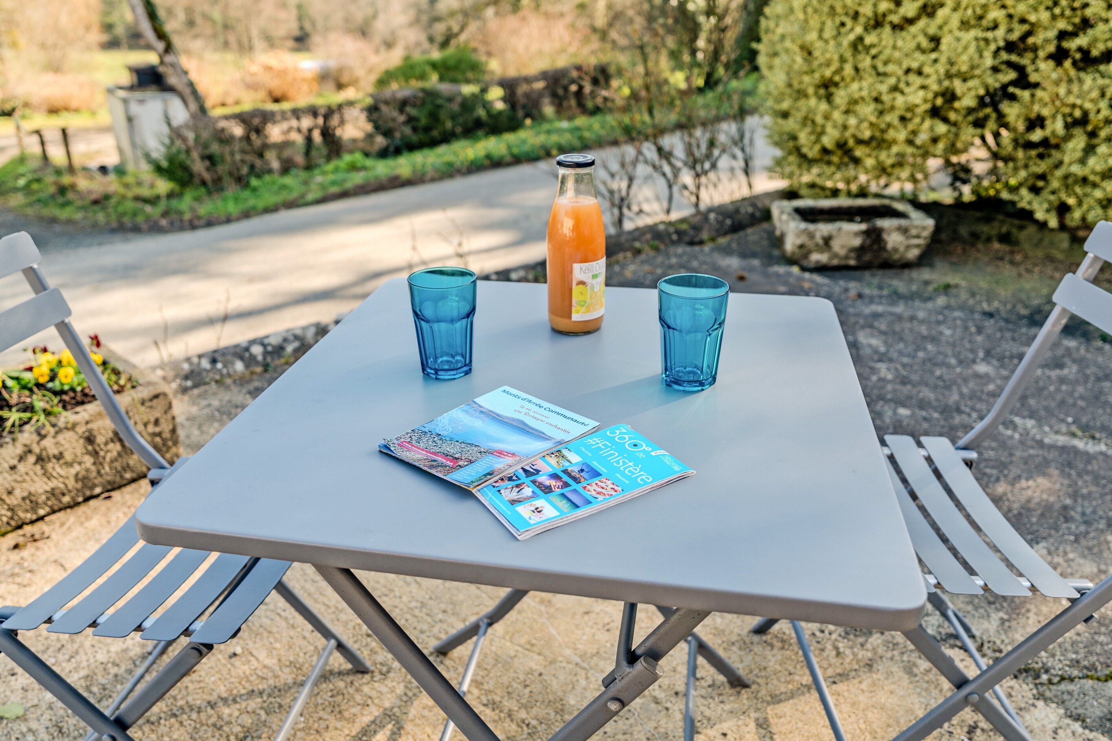 A table with a bottle and two glasses, a magazine, and a metal chair.