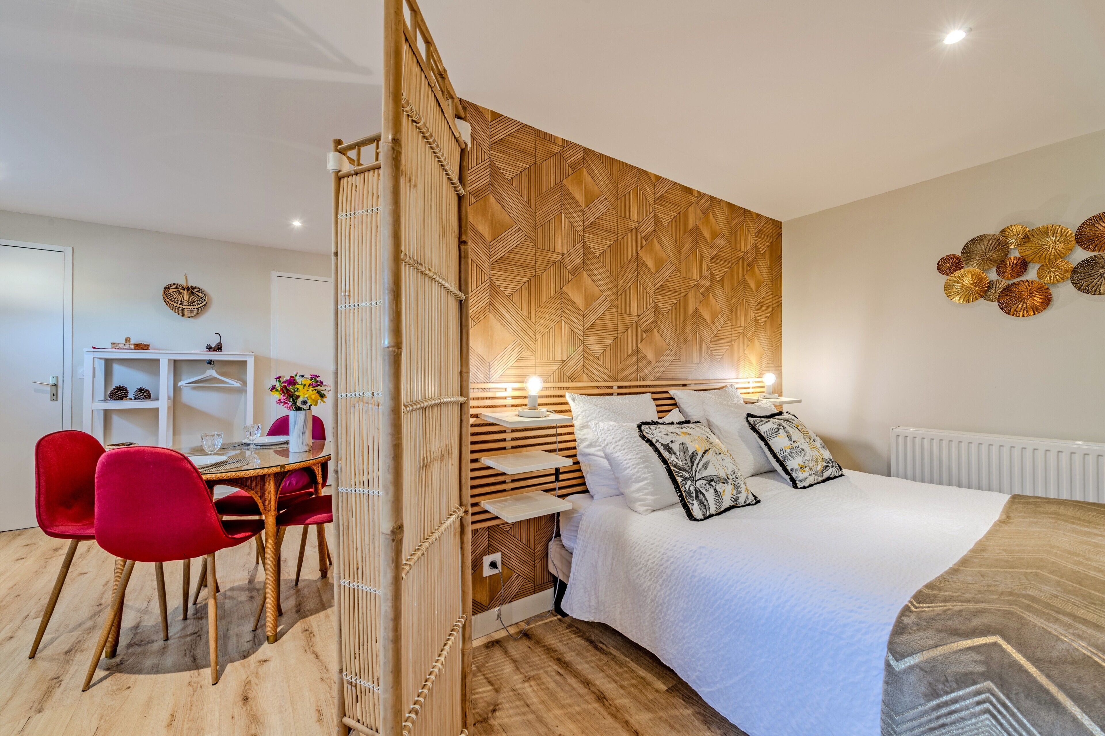A modern bedroom with a bed, bedside table, lamp, and a dining area with chairs and a table.