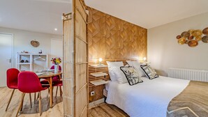 A modern bedroom with a bed, bedside table, lamp, and a dining area with chairs and a table. - Studio Apartment 'Le Grand Large' with Shared Terrace, Shared Garden and Wi-Fi (Lopérec)