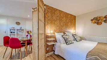 Un dormitorio moderno con cama, mesita de noche, lámpara y un área de comedor con sillas y mesa.