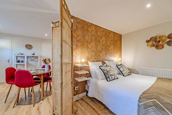 A modern bedroom with a bed, bedside table, lamp, and a dining area with chairs and a table.