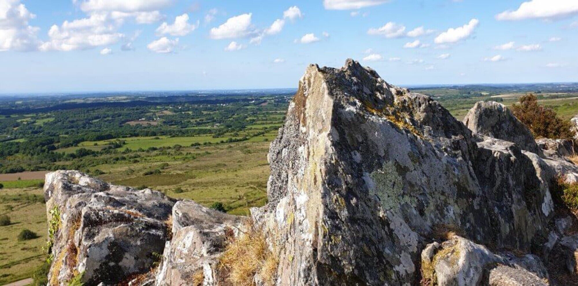 En klippeformation med panoramaudsigt over en grøn dal og fjerne bakker.