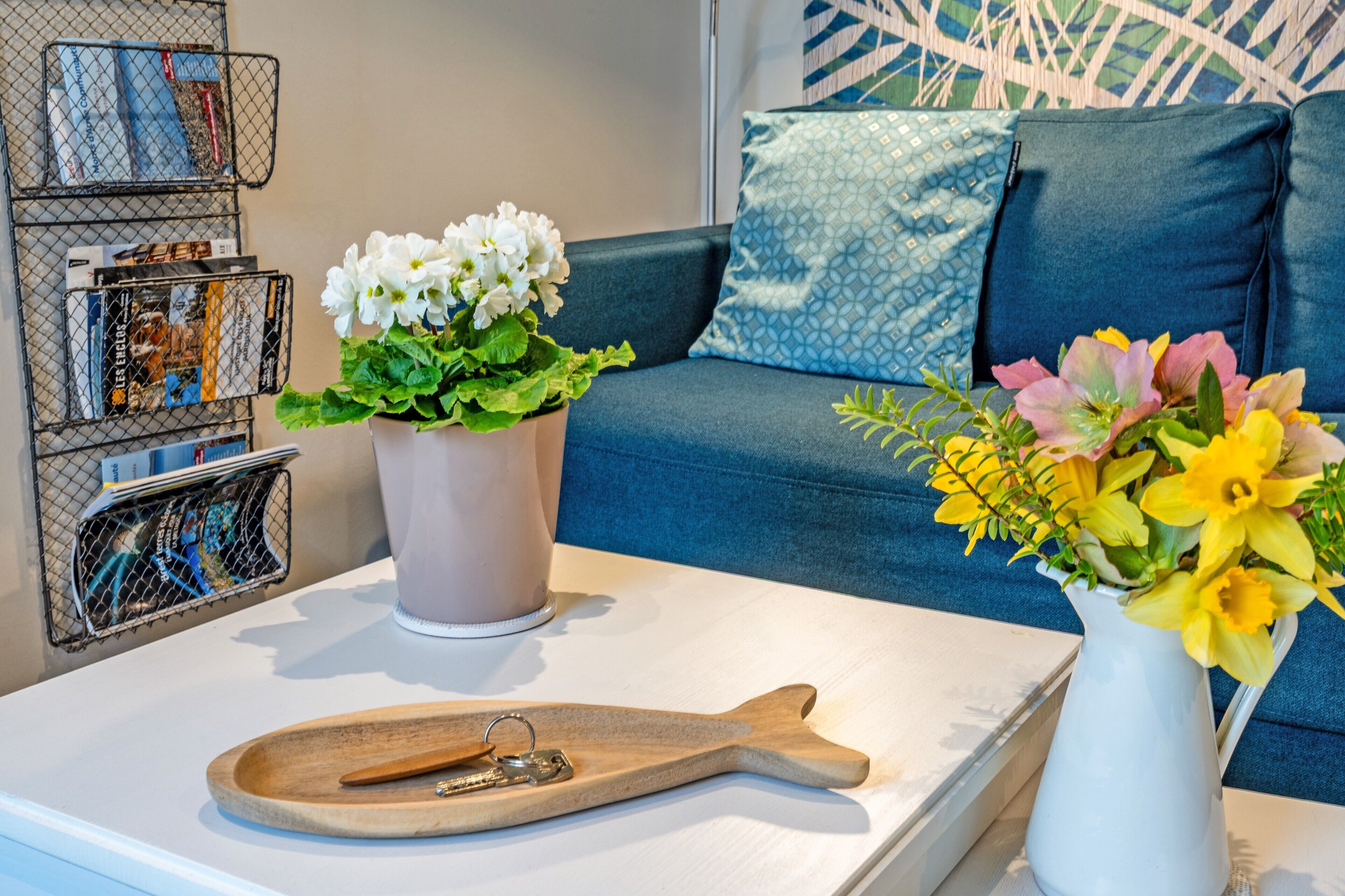 Ein weißer Couchtisch mit einer Holztablett, eine weiße Vase mit weißen Blumen und eine weiße Vase mit gelben Blumen.