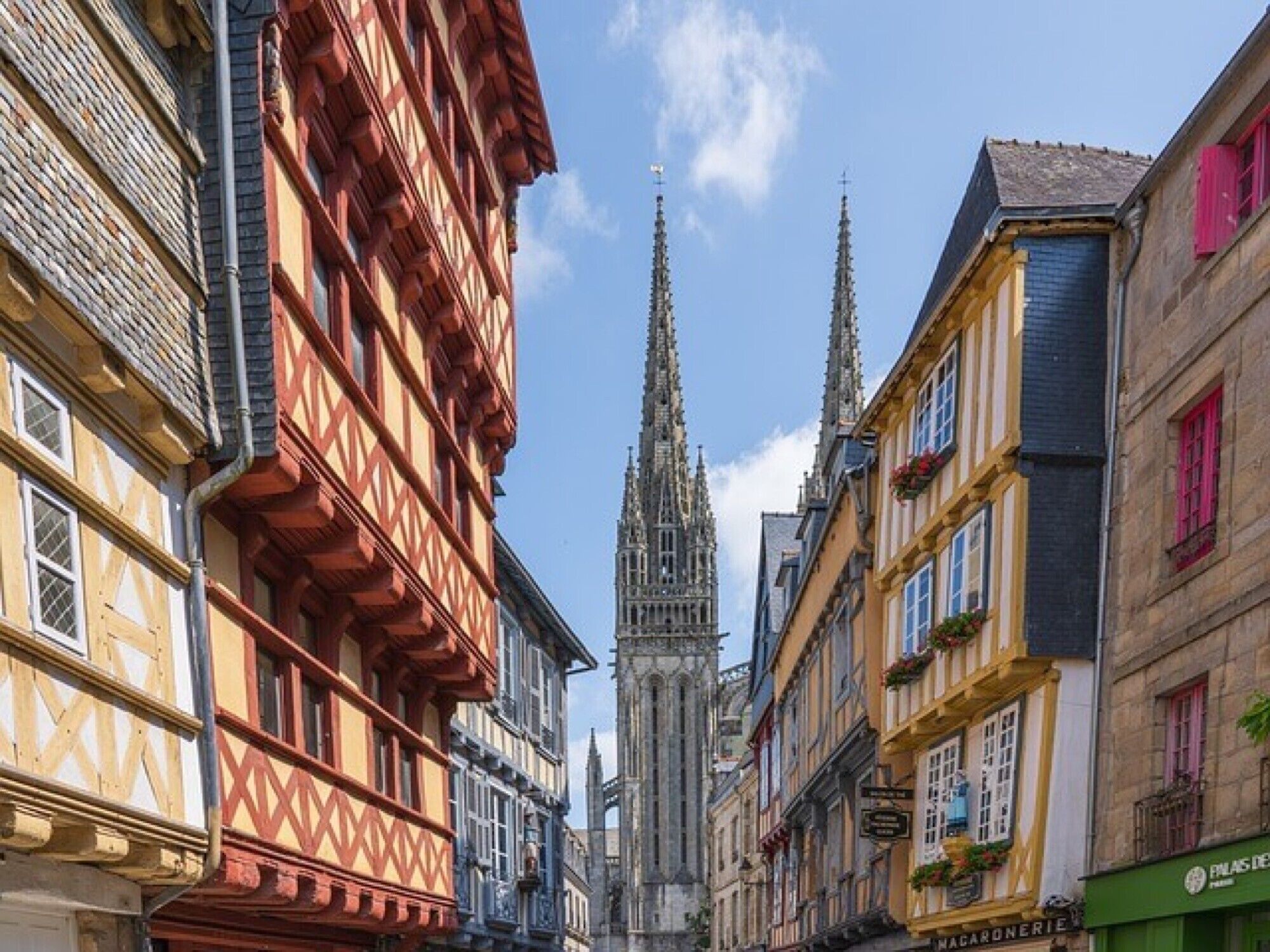 Une rue bordée de bâtiments traditionnels à colombages, avec une cathédrale gothique en arrière-plan.
