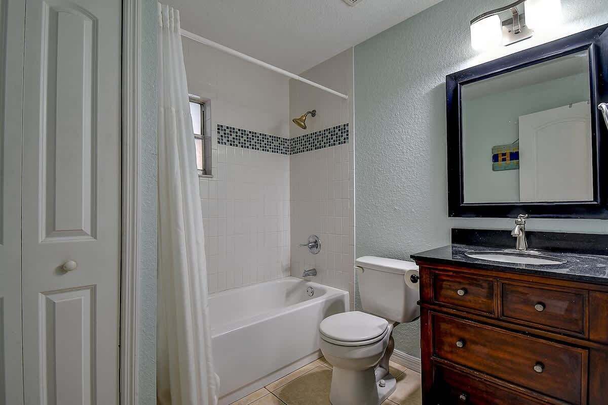 A bathroom with a bathtub, toilet, and vanity with a mirror.