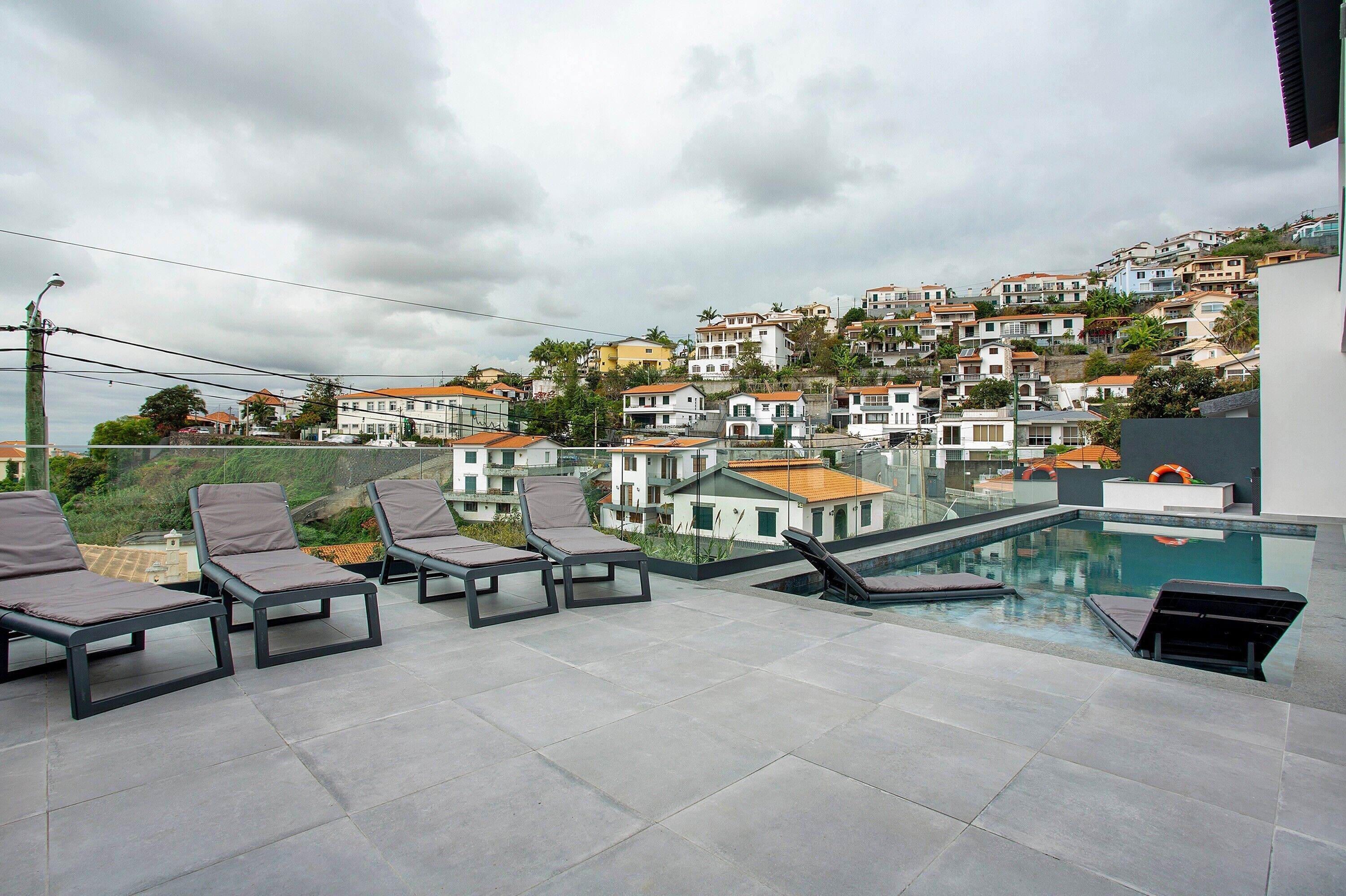 Eine Dachterrasse mit Liegestühlen, einem Pool und Blick auf eine Wohngegend am Hang.