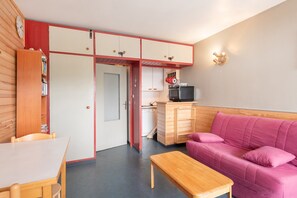 A compact room with a kitchenette, a dining area, and a pink sofa.