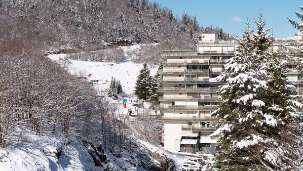 Un edificio de varios pisos con un diseño arquitectónico moderno, rodeado de árboles nevados y un paisaje montañoso.