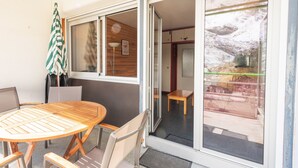 Una habitación con una mesa y sillas de madera, un paraguas a rayas y un ventanal corredera que da a un espacio exterior.