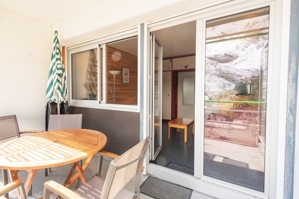 A room with a wooden table and chairs, a striped umbrella, and a sliding glass door leading to an outdoor area.