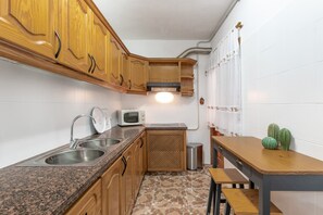 A kitchen with wooden cabinets, a granite countertop, a microwave, a sink, and a trash can.