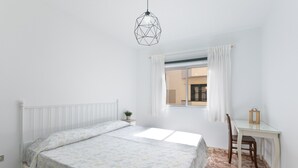 Un dormitorio con cama, escritorio, silla, lámpara colgante y ventana con cortinas.