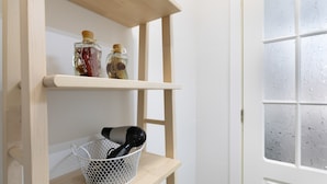 Interior blanco con repisa de madera que sostiene dos botellas de vidrio y una cesta blanca con un secador de pelo.