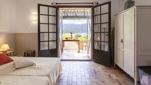Une chambre avec un lit, une table de chevet, un bureau et une porte ouverte donnant sur un balcon avec vue sur la mer.