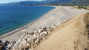 Une plage bordée de rochers, avec une eau d’un bleu limpide et des montagnes qui se dessinent à l’horizon.