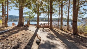 A wooden deck with a bench, a rope swing, and a view of a lake surrounded by trees. - Water's edge, enjoy this lakefront property. (Big Bear Lake)
