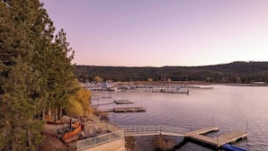 A lakeside dock with a wooden deck and seating area, surrounded by trees and a distant forest. - Water's edge, enjoy this lakefront property. (Big Bear Lake)