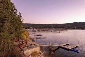 A lakeside dock with a wooden deck and seating area, surrounded by trees and a distant forest. - Water's edge, enjoy this lakefront property. (Big Bear Lake)