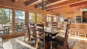 A wooden interior with a dining table, chairs, a chandelier, and a kitchen area. - Water's edge, enjoy this lakefront property. (Big Bear Lake)