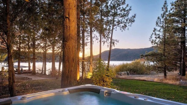 A hot tub surrounded by trees with a view of a lake and mountains in the background. - Water's edge, enjoy this lakefront property. (Big Bear Lake)