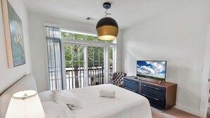 Habitación de hotel con cama, televisor, escritorio y balcón con vistas a árboles.