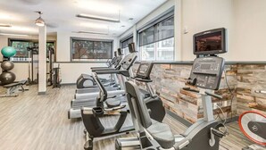 Een fitnessruimte met loopbanden, trainingsballen en een televisiescherm.