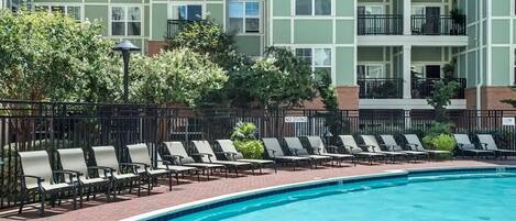 A swimming pool with lounge chairs and a building with balconies in the background.