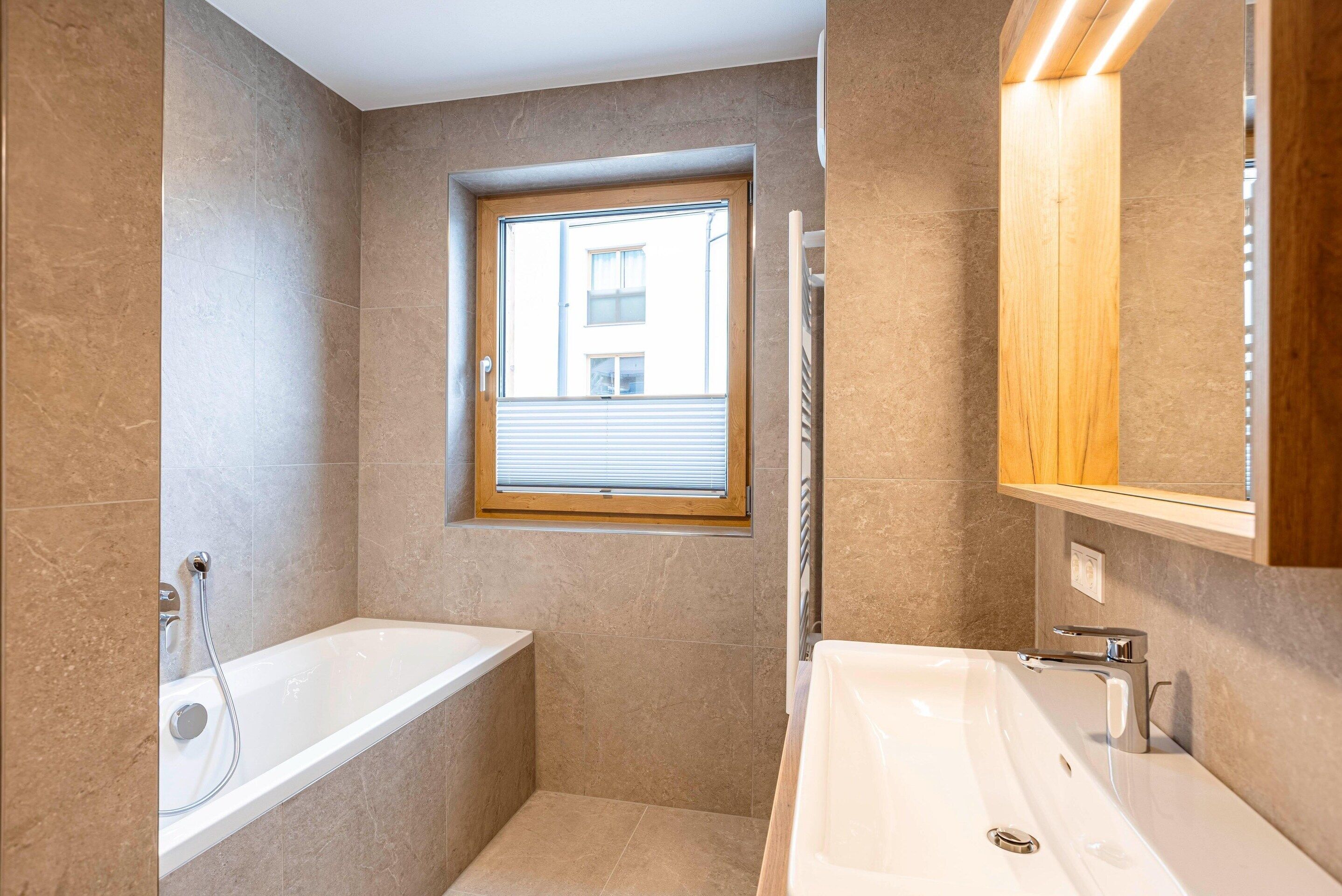 A modern bathroom with a bathtub, a sink, and a window with blinds.